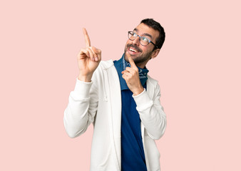 Handsome man with glasses pointing with the index finger and looking up on isolated pink background