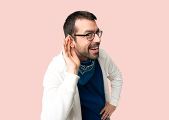 Handsome man with glasses listening to something by putting hand on the ear on isolated pink background