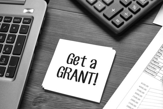 Desk with business accessories, calculator, documents with charts, fountain pen, laptop and paper for notes with text Get a grant