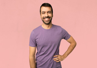 Handsome man posing with arms at hip and smiling on isolated pink background