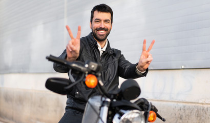 Fototapeta na wymiar Young man on a motorbike making victory gesture