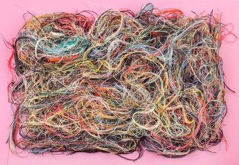 Colorful tangled threads on pink background. Closeup.