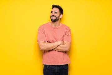 Handsome man over yellow wall looking up while smiling