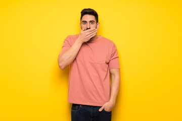 Handsome man over yellow wall covering mouth with hands for saying something inappropriate