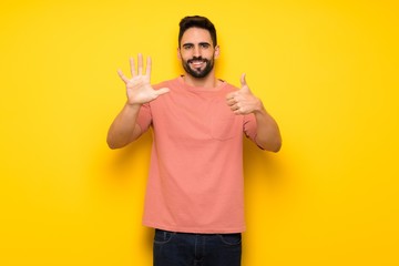 Handsome man over yellow wall counting six with fingers