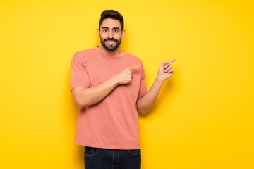 Handsome man over yellow wall frightened and pointing to the side