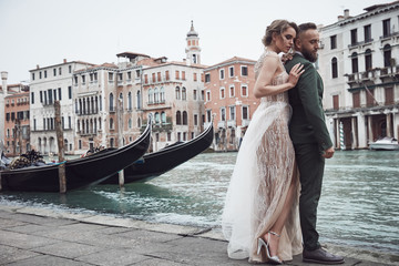 Amazing wedding couple near the canal in Venice. Elegant woman in luxury ivory dress, messy updo hair, man in green three-piece suit