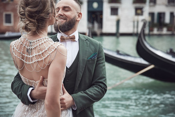 Wedding couple near the canal in Venice. Elegant woman in luxury ivory dress, messy updo hair, man in green three-piece suit - 249339728