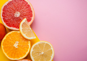 Flat lay of cut ripe juicy grapefruit, lemon and orange on pink and yellow background with copyspace.