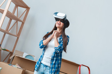 Young woman moving to a new place standing looking in virtual reality headset smiling excited