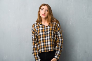 Naklejka premium Young redhead girl over grunge wall is a little bit nervous and scared pressing the teeth