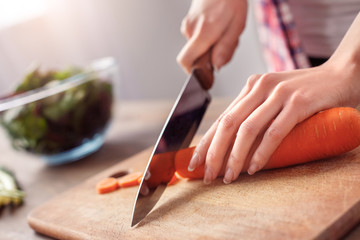 Young girl at kitchen healthy lifestyle standing cutting carrot on board close-up