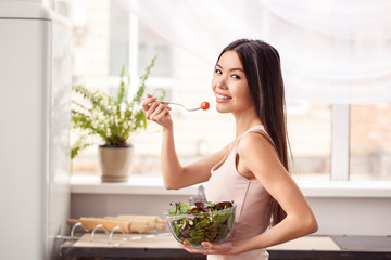 Young girl at kitchen healthy lifestyle walking with bowl and tomato on fork looking back playful
