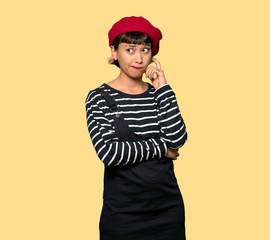 Young woman with beret with confuse face expression while bites lip over yellow background