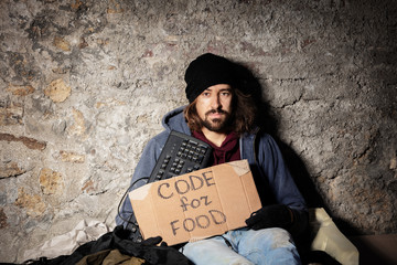 Man sits on floor with keyboard and cardboard sign