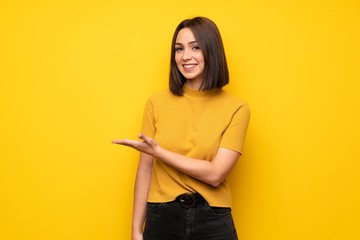 Young woman over yellow wall presenting an idea while looking smiling towards