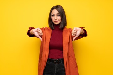 Young woman with coat showing thumb dowg with negative expression