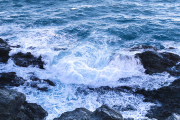 Waves crashing against rocks in a sea forming white foam. Windy day