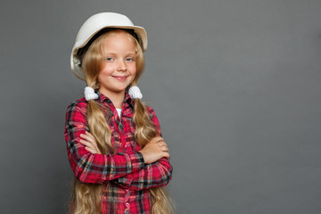 Little girl with ponytails in helmet standing isolated on grey crossed arms looking camera playful