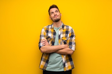 Handsome man over yellow wall looking up while smiling