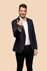 Handsome business man inviting to come with hand. Happy that you came over ocher background