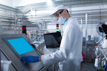 man in a white robe and a mask with a laptop in his hands stands near the digital screen at the factory