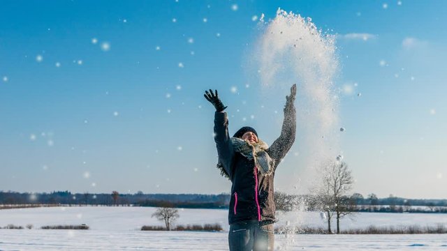 cinemagraph of a young girl having fun, throwing up the snow to the blue sky in winter. snow flakes are falling