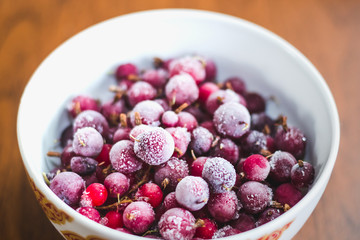 A mixture of red frozen berries of currant and gooseberry covered with white frost in a white plate on the table.