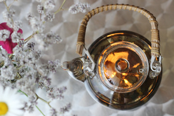 glass teapot for brewing elite tea on a glass heated stand on a light background with flowers