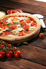 Pizza with tomatoes, mozzarella cheese, black olives and basil. Delicious italian pizza on wooden pizza board.