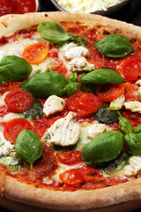 Pizza with tomatoes, mozzarella cheese, black olives and basil. Delicious italian pizza on wooden pizza board.