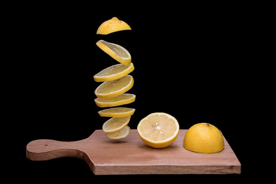 Halved and sliced lemons on a wooden chopping board with a black background