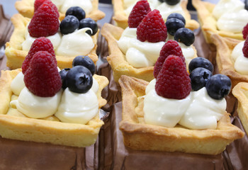 pastries with cream and raspberry with blueberries for sale in a