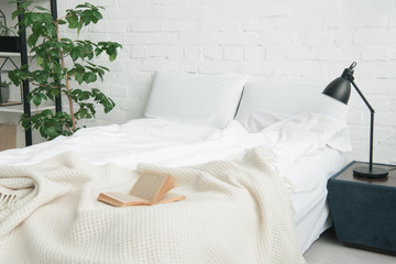 book on white bed, plant and lamp on black nightstand