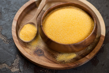 Wooden bowl with raw polenta on a wooden serving tray, horizontal shot