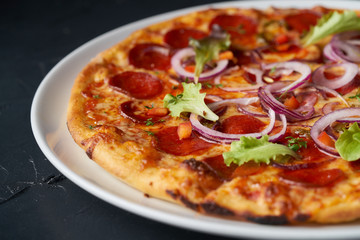 Fresh italian salami hot pizza with green leaves on black organic background top view close up