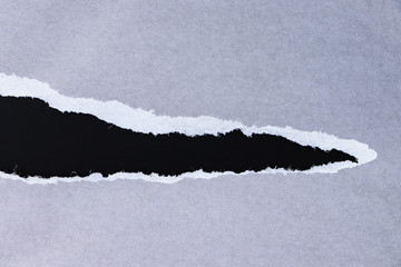 Ragged edge of gray paper on black surface. Empty background.