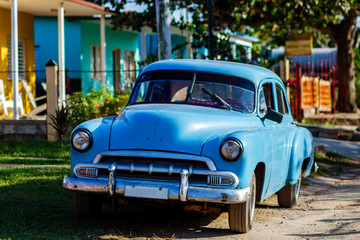 Blue vintage Cuban car parked in front of tropical home in rural Cuba