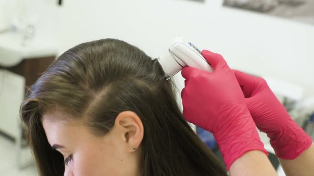 doctor dermatologist diagnoses the structure of the hair of a young pretty girl with a special tool - a trichoscope. Trichology, trichogram