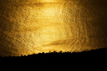 Golden sunset reflection in the ocean near dark coastline