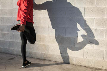 Cast shadow of athlete stretching quadriceps during running urban workout.