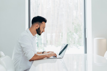Fototapeta premium Concentrated brunette man in white shirt typing on laptop keyboard