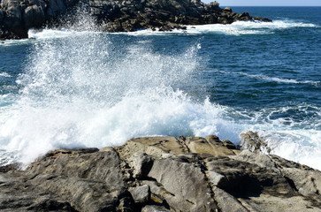 Wild waves splashing against the rocks. Blue sea with white foam. Galicia, Spain, blue sky, sunny day.