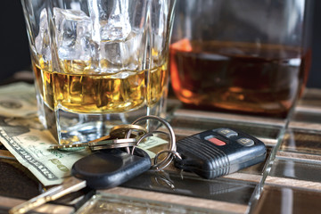 Alcohol in a glass with ice, bottle in the background.  Keys and money in foreground.  Suggestive of drinking and driving.