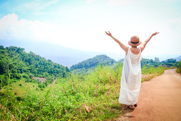 Women tourists Wear a white hat and stand behind. Raise two hands fresh air at the top of the mountain.