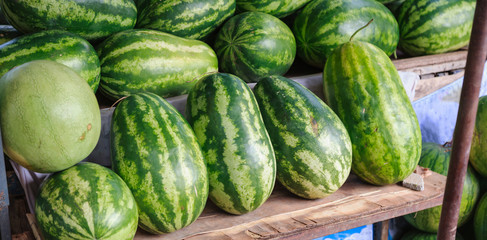 Fresh, sweet, natural farm grown, watermelon tropical organic fruits with hard green rinds, reddish juicy flesh and many black seeds in nature. Seasonal, Summer Asian fruit on street food market stall