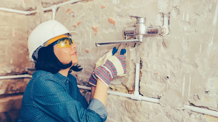 Female construction worker with wrenches repairs the pipes in the bathroom