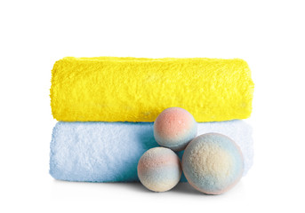 Stack of clean soft towels and bath bombs on white background