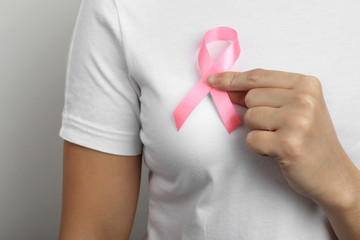 Woman holding pink ribbon on grey background, closeup. Breast cancer awareness