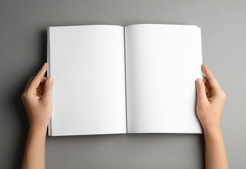 Woman holding brochure with blank pages on grey background, top view. Mock up for design